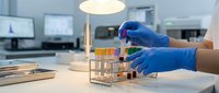 Laboratory technician in blue gloves handling test tubes with colorful samples in modern research facility for scientific analysis and experimentation.