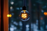 Glowing round light bulb with warm filament illuminated against dark blurred background with bokeh lights creating cozy atmospheric mood.