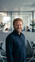 Confident middle-aged Caucasian businessman with curly hair and beard smiling in modern office environment for corporate leadership and success concepts.