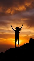 Woman silhouette with raised arms celebrating freedom on mountain peak against dramatic orange sunset sky with flowing hair and victory pose.