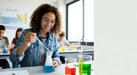 Young African American female student conducting chemistry experiment with colorful liquids in modern laboratory classroom setting.