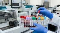 Laboratory technician in blue gloves holding test tube rack with colorful blood samples in modern medical research facility for diagnostic testing.
