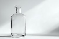 Empty transparent glass bottle with round shoulders and narrow neck casting soft shadow on white surface in minimalist composition with diagonal light.