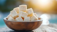 Fresh Turkish delight cubes dusted with powdered sugar served in rustic wooden bowl on weathered table surface with soft natural lighting and blurred background.