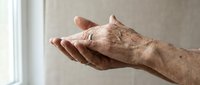 Senior adult male hand with age spots and wrinkles extended in open palm gesture against neutral background, representing aging, care, giving, or receiving assistance.