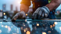Close-up of worker hands installing solar panel at sunset with bokeh light reflections and urban cityscape background creating atmospheric scene.