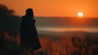 Silhouette of person in coat standing on hill overlooking misty valley during golden sunrise, contemplative mood for wellness and mindfulness content.
