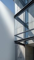 Modern office building facade with glass windows and steel frame architectural details creating geometric shadows on white exterior wall.
