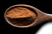 Ground cinnamon powder in wooden spoon macro photography on black background, aromatic spice for baking and cooking, natural food ingredient.