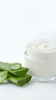 Natural aloe vera cream in glass jar with fresh cut aloe leaves on white background for skincare and cosmetic products.