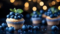 Fresh blueberry cupcake topped with ripe berries and mint leaves on dark wooden surface with golden bokeh lights in background, selective focus.