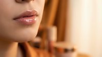 Close-up of woman's glossy pink lips with natural makeup in warm golden lighting for beauty and cosmetics advertising campaigns.