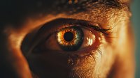 Close-up macro shot of human eye with golden sunlight reflection, showing detailed iris pattern, eyelashes and skin texture in warm amber tones.