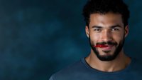 Young African American man with beard smiling confidently against dark blue background, wearing casual t-shirt, displaying genuine warmth and optimism in professional portrait.