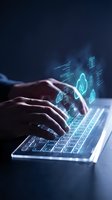Hands typing on laptop with glowing cybersecurity holographic interface displaying shield icons and digital protection elements in blue light.