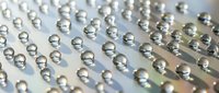 Rows of clear water droplets creating perfect spheres on reflective surface with soft lighting and shallow depth of field for modern design projects.