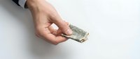 Male hand holding crumpled dollar bill against white background, representing financial loss, money problems, or economic hardship in business and personal finance contexts.