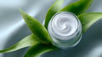 Luxurious white cosmetic cream in glass jar with fresh green leaves on silk background, natural organic skincare and beauty product photography.
