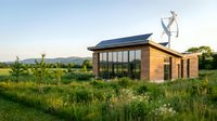 Modern eco-friendly house with solar panels and wind turbine in green meadow at sunset. Sustainable architecture with large windows and natural materials.