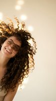 Happy young woman with curly hair laughing joyfully against warm bokeh lights background expressing genuine happiness and positive emotions.