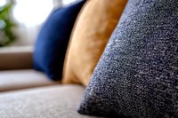 Soft decorative pillows in navy blue, gray and mustard yellow on modern sofa, close-up view with selective focus showing textured fabric detail.