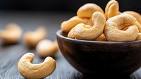 Fresh roasted cashew nuts in wooden bowl on dark background, selective focus on foreground nut, macro food photography with copy space.