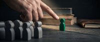 Male hand stopping falling dominoes with green wooden peg, representing leadership, risk management, and crisis prevention in business strategy and decision-making scenarios.