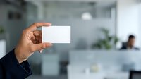 Male professional of South Asian descent holding blank white business card in modern office environment, suitable for corporate branding, business identity, and professional networking materials.