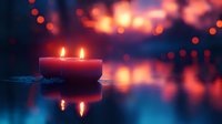 Red candles burning with soft flame reflection on water surface against blurred bokeh lights creating romantic atmospheric mood for meditation or celebration.
