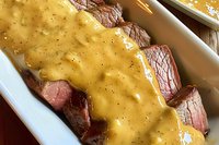 Sliced medium-rare beef tenderloin covered in creamy mustard sauce with black pepper, served on white platter. Close up view of gourmet meat dish.