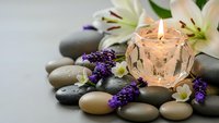 Spa wellness composition with burning candle, smooth stones, white lilies and purple lavender flowers for relaxation and meditation therapy.
