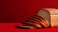 Freshly sliced loaf of homemade bread on vibrant red background, showcasing texture and wholesome appearance for food marketing.