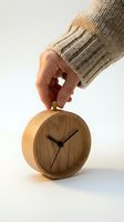 Hand in cozy knit sweater adjusting a round wooden desk clock with black hands on a white background.
