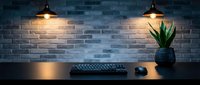 Modern workspace with industrial pendant lights illuminating brick wall, wooden desk featuring keyboard, mouse and potted plant creating cozy office atmosphere.