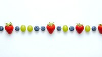 Fresh berries and grapes arranged in colorful row pattern on white background for healthy eating and nutrition concepts.