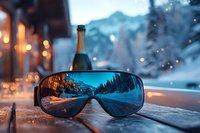 Ski goggles reflecting winter mountain landscape at sunset with champagne bottle in background, creating cozy alpine atmosphere on wooden terrace.