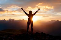 Woman celebrating success on mountain peak at golden sunrise with arms raised in victory pose against dramatic sky and mountain ranges.