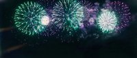 Spectacular colorful fireworks display bursting in night sky with green, purple and white explosions creating magical celebration atmosphere.