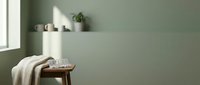 Cozy bedroom corner with wooden stool, folded beige blanket, glass of water, potted plant on shelf, and soft natural light from window against sage green wall.