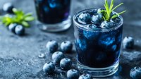 Fresh blueberry cocktail with ice cubes, rosemary garnish and scattered berries on dark background. Refreshing summer drink with natural ingredients.