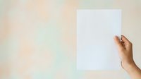 Hand holding blank white card or paper against soft blurred background, suitable for mockups, presentations, and advertising campaigns.