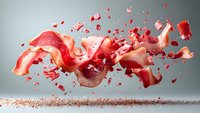 Dynamic explosion of red rose petals captured in mid-air against gray background, with scattered particles creating dramatic motion and depth in studio lighting.