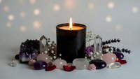 Black candle burning surrounded by healing crystals amethyst quartz and dried lavender flowers creating peaceful meditation spa atmosphere with bokeh lights.