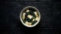 Traditional Japanese miso soup with tofu cubes and wakame seaweed in ceramic bowl on dark wooden background for authentic Asian cuisine presentation.