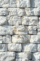 White limestone wall with rough textured blocks stacked in rows creates rustic architectural detail. Natural stone surface shows weathered cracks and irregular shapes.