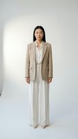 Young East Asian woman wearing neutral beige blazer over white shirt and cream wide-leg trousers, standing against white background. Corporate fashion and business attire.