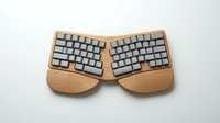 Ergonomic split keyboard with wooden frame and gray keys on white background, suitable for typing, workspace design, and office equipment concepts.