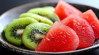 Fresh juicy watermelon wedges and sliced kiwi fruit arranged in black ceramic bowl, macro food photography showing vibrant colors and texture of summer fruits.