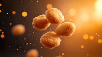Crispy golden chicken nuggets floating in warm atmospheric lighting with bokeh effects and particles, dramatic food photography on dark background.