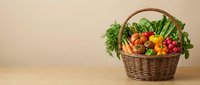 Fresh organic vegetables in wicker basket on wooden table including carrots tomatoes peppers and leafy greens for healthy cooking and nutrition.